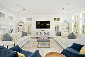 A spacious living room with a large flat-screen TV, white sofas, and a coffee table. - 🏖️ Caspian Blue Cottage | Beach Access, Pool, Bikes & Screened Porches 🚲 (Inlet Beach)