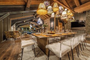 Un comedor amplio con una larga mesa de madera dispuesta para una comida, rodeado de sillas transparentes.
