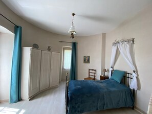 Une chambre à coucher comprenant un lit, une armoire, une table de chevet, une lampe, un tableau au mur et un ventilateur de plafond.