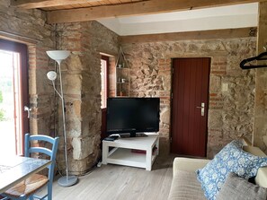 Una habitación con una televisión sobre un soporte blanco, una silla azul, una mesa blanca y un sofá con cojines estampados.