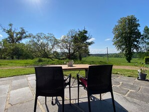 Un patio exterior con una mesa y dos sillas, un regadera y una planta en maceta.