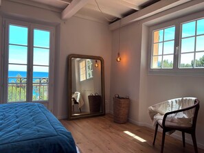 Une chambre à coucher avec un grand lit, une chaise, un miroir et deux fenêtres donnant sur un beau paysage.