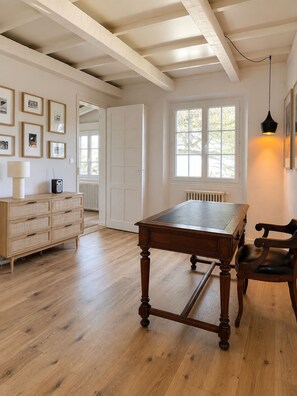Une pièce avec une table en bois, une chaise, une commode et des tableaux encadrés accrochés au mur.