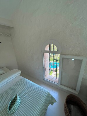 Une chambre à coucher avec un lit, une fenêtre donnant sur une piscine et une petite fenêtre grillagée.