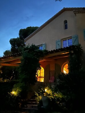 Un immeuble de deux étages doté d’un balcon et dont l’intérieur est éclairé d’une lumière chaleureuse, visible à travers les fenêtres.