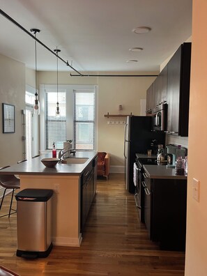 Een moderne keuken met een centraal eiland, roestvrijstalen apparatuur en een eethoek met een stoel en tafel.