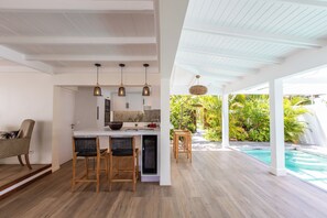 Eine moderne Küche mit weißer Arbeitsplatte, Holzstühlen und Pendelleuchten.