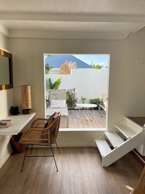 Ein Zimmer mit Holzboden, einem Korbstuhl, einem weißen Schreibtisch und einem Fenster mit Blick auf einen Garten.