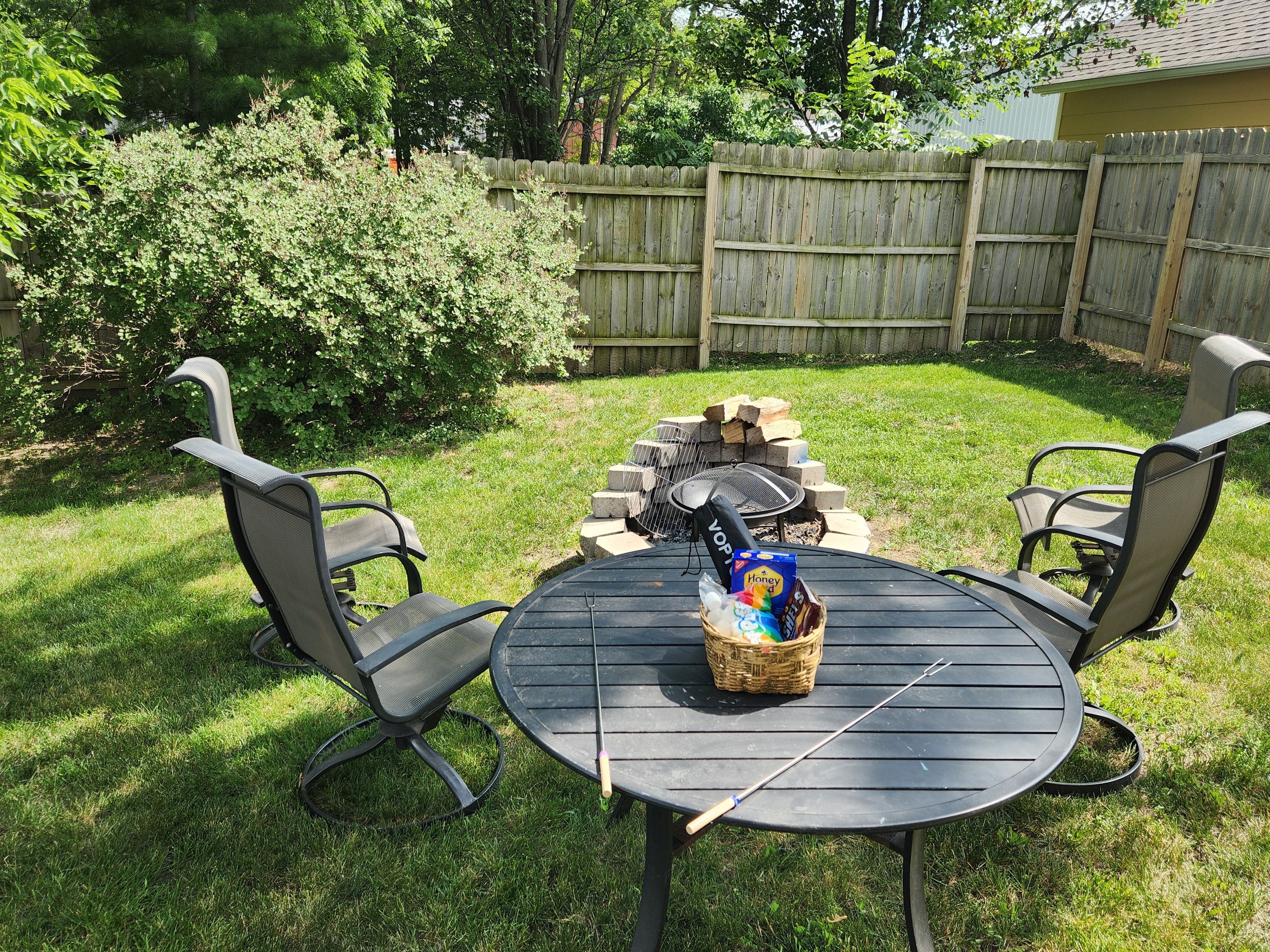 Ein Garten mit einem runden Tisch, zwei Stühlen, einer Feuerstelle und einer Snack-Korb.