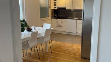 Una cocina moderna con armarios blancos, un refrigerador de acero inoxidable y un comedor con mesa y sillas blancas.