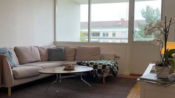 A modern living room with a sofa, coffee table, and a view of a building through large windows.