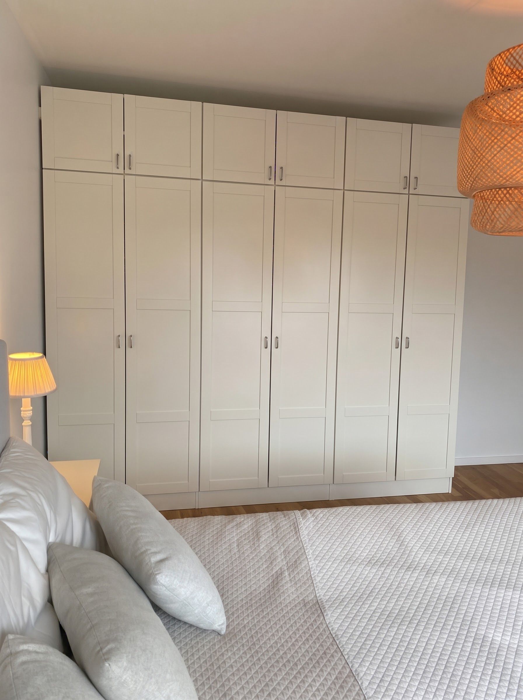 Un dormitorio con un armario grande, una cama con almohadas, una lámpara de noche y una alfombra con textura.