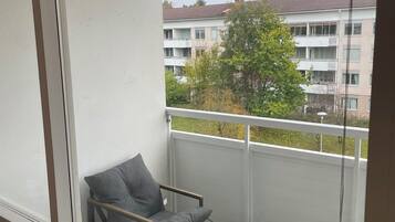 Un balcón con un sofá gris y una mesita, con vistas a una zona residencial con edificios y árboles.