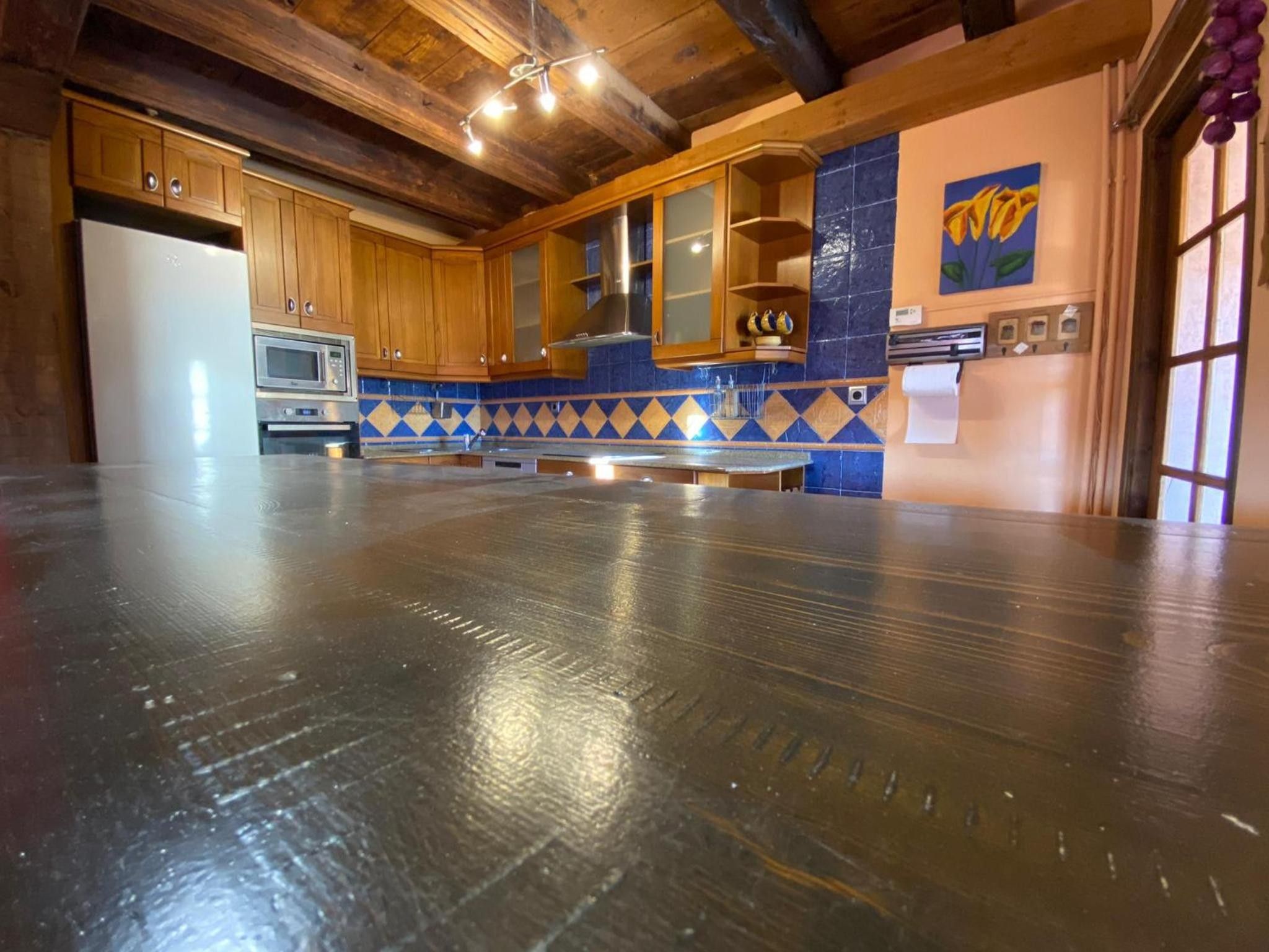 A spacious kitchen with wooden cabinets, a stainless steel refrigerator, and a blue and yellow tiled backsplash.