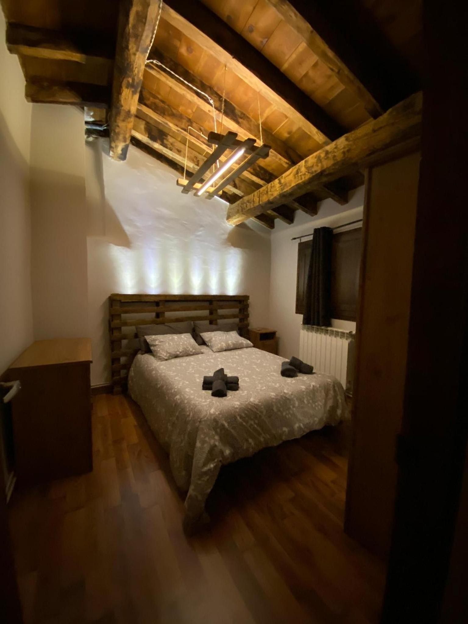 A bedroom with a wooden ceiling, a bed with a white bedspread, a nightstand, and a radiator.