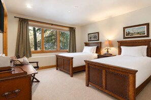 Quarto de hotel com duas camas, uma escrivaninha, uma cadeira, janela com cortinas e um quadro na parede.