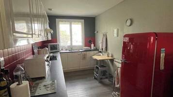 A kitchen with a red refrigerator, white cabinets, a window, and a clock on the wall.