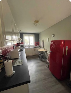 A kitchen with a red refrigerator, white cabinets, a window, and a clock on the wall.