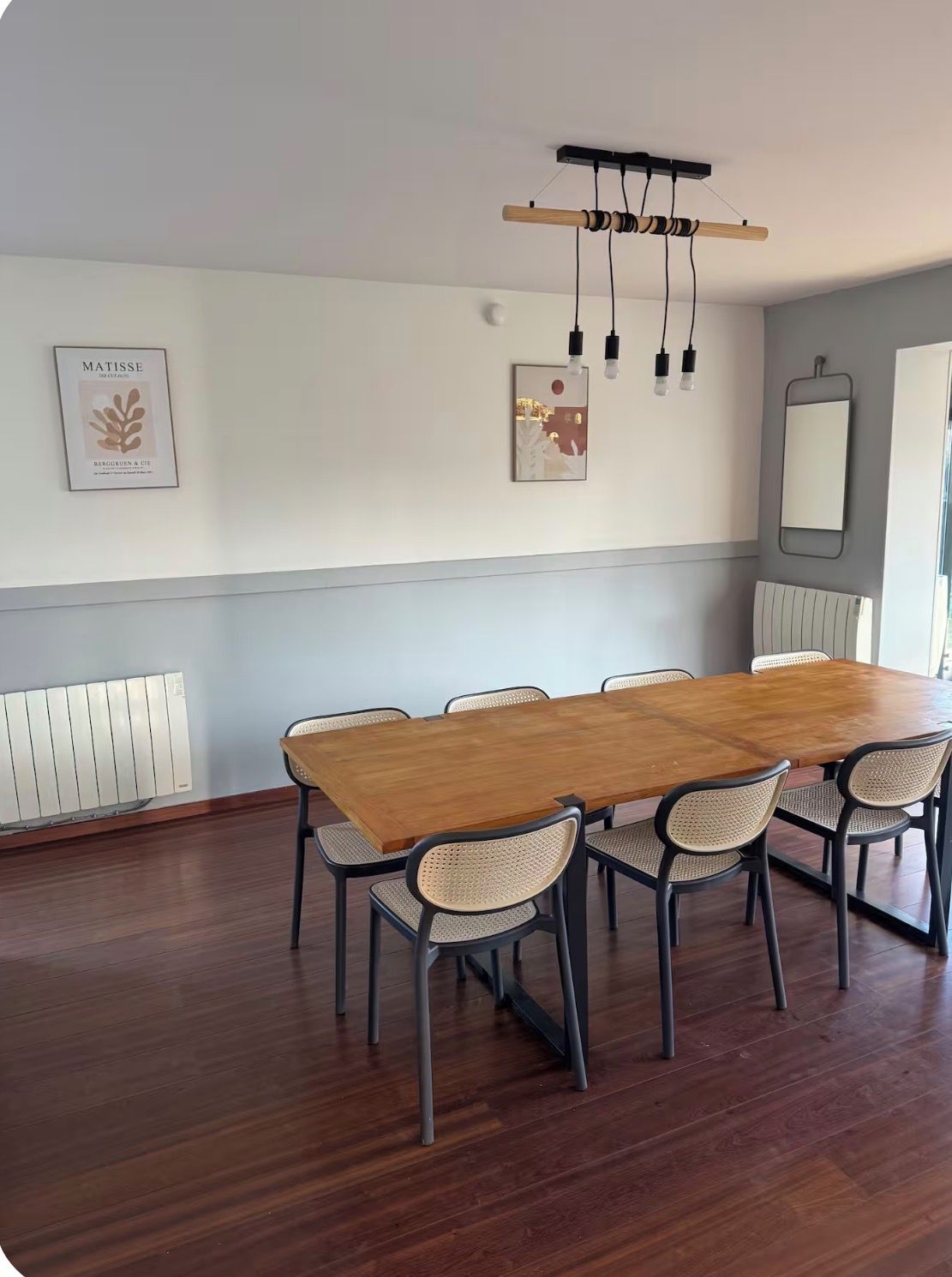 A dining area with a wooden table and six chairs, a radiator, and wall-mounted artwork.
