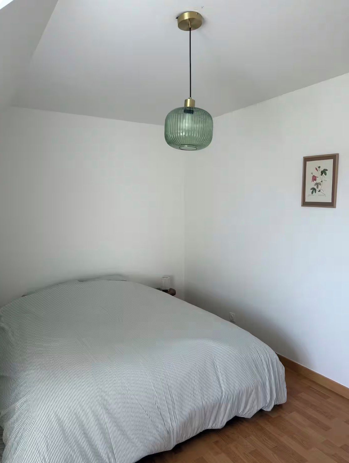A bedroom with a bed, a hanging light fixture, and a framed picture on the wall.