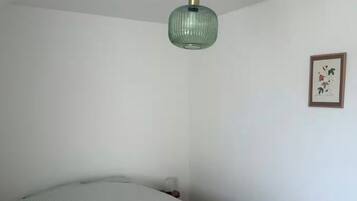 A bedroom with a bed, a hanging light fixture, and a framed picture on the wall.