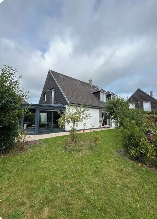 A modern house with a sloped roof, a glass conservatory, and a well-maintained lawn.