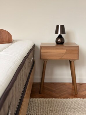 Un lit avec une tête de lit en bois, une petite table de chevet en bois avec une lampe, et un parquet à motifs en chevrons.