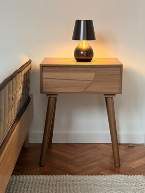 Une table de chevet en bois avec une lampe, placée à côté d’un lit doté d’une tête de lit.