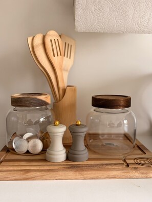 Une planche à découper en bois, un bocal en verre, un ensemble de cuillères en bois et deux salières et poivrières.