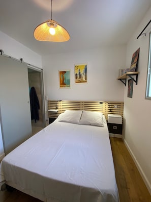 Ett sovrum med en säng, en hängande lampa, ett nattduksbord, en vägghylla och en dörr.