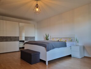 A modern bedroom with a bed, bedside tables, a bench, and a hanging light fixture. - New Listing (Lügde)