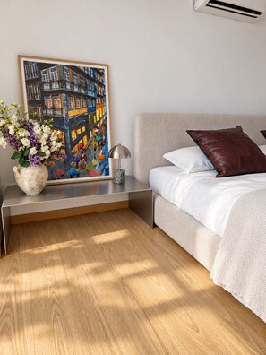 Une chambre à coucher avec un lit, une table de chevet, une lampe, un vase de fleurs et un tableau au mur.