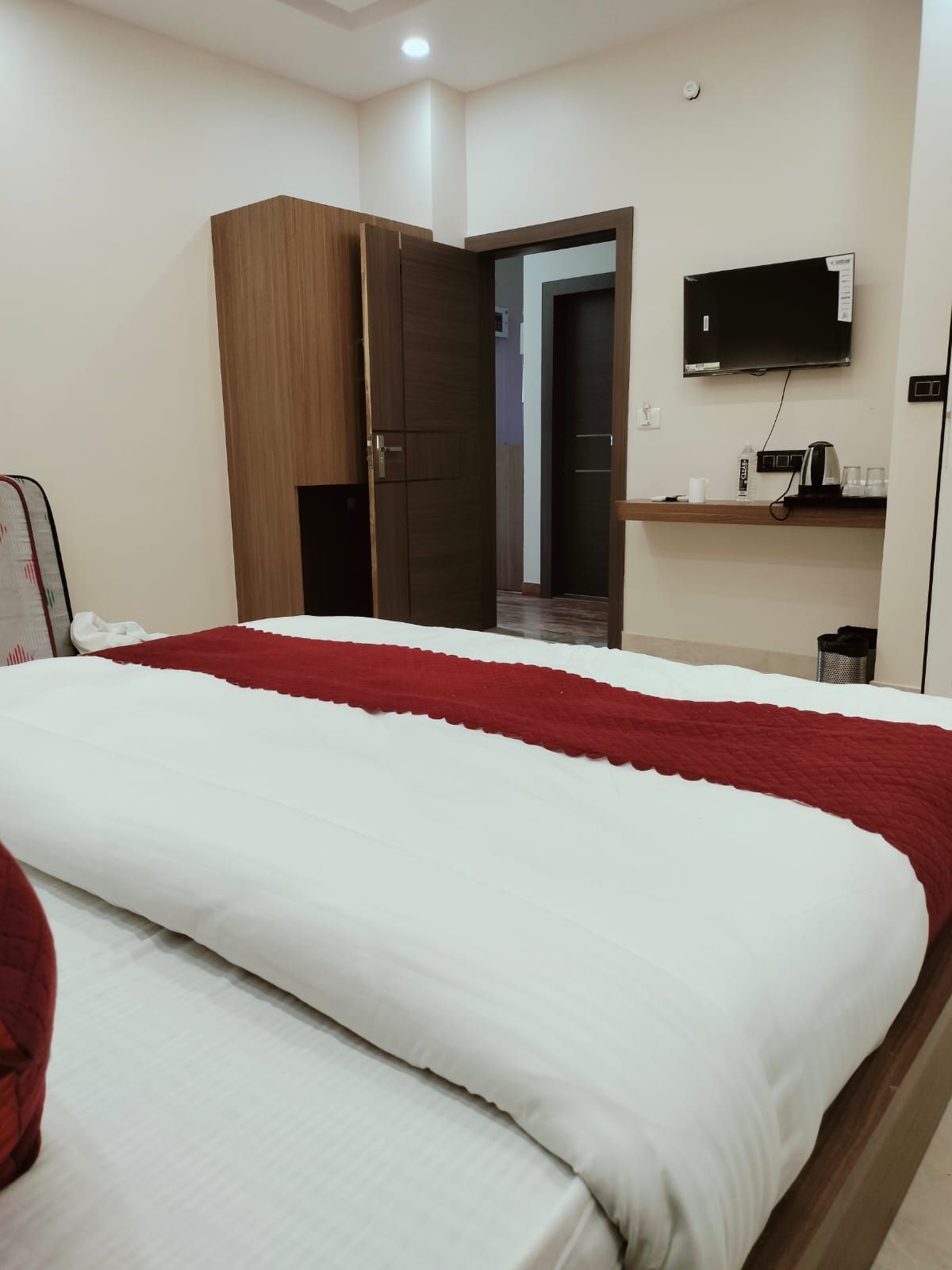 Una habitación de hotel con una cama, un armario, un televisor y un estante con objetos.