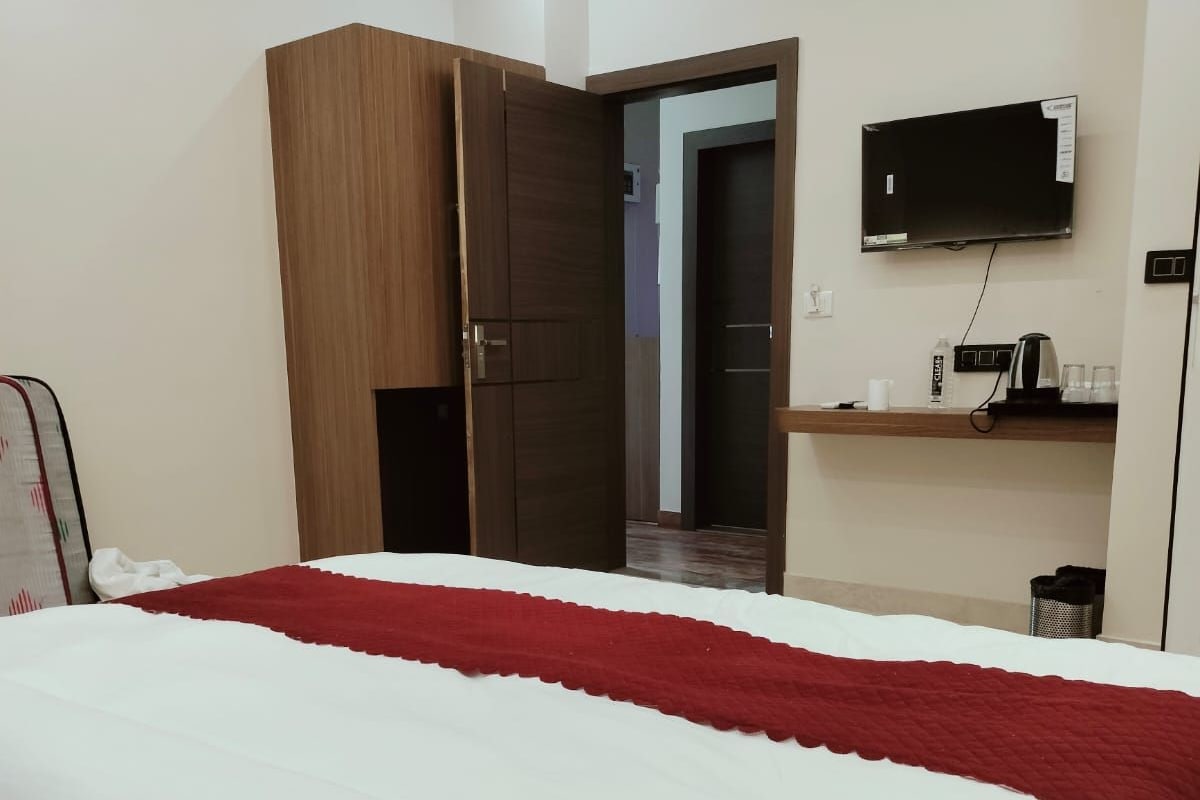 A hotel room with a bed, a wardrobe, a television, and a small shelf with items.