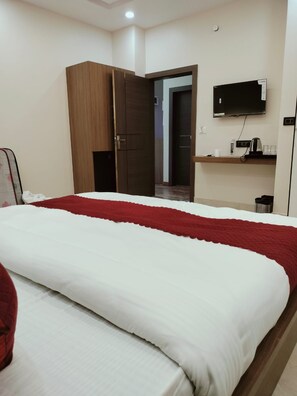 A hotel room with a bed, a wardrobe, a television, and a small shelf with items. - Hotel Aastha Grand (Varanasi)