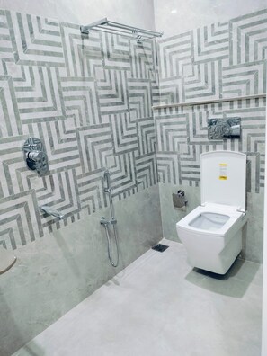 A bathroom with a shower, toilet, and a patterned wall. - Hotel Aastha Grand (Varanasi)