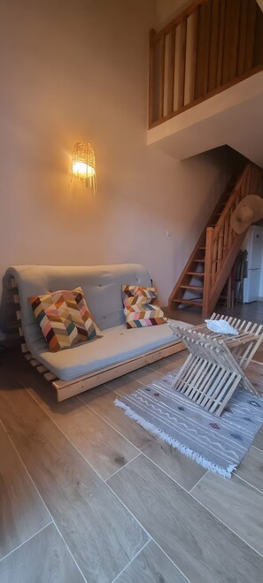 En moderne stue med sofa, mønstrede puder, vægmonteret lampe, en trætrappe og et mønstret tæppe.