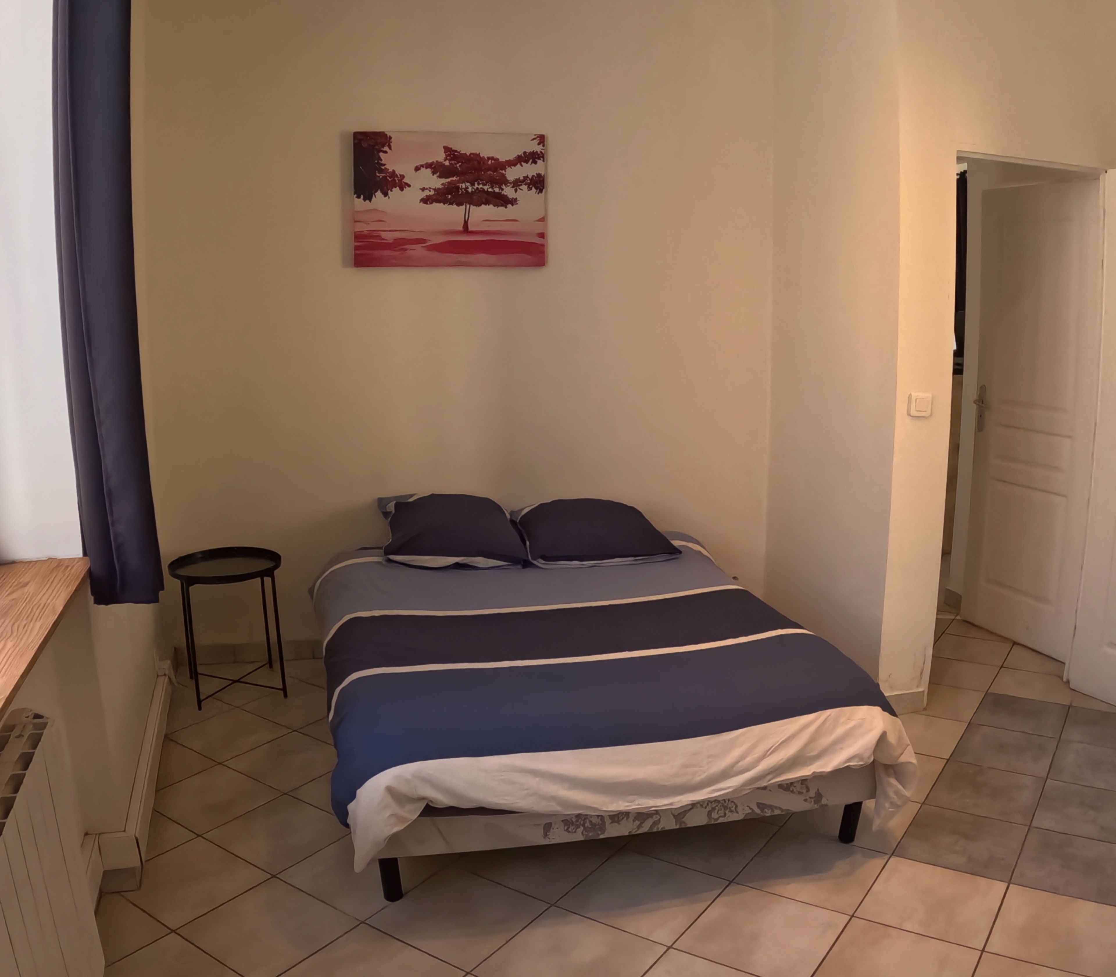 Une chambre à coucher avec un lit, une petite table et un tableau accroché au mur.