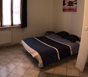 Ein Schlafzimmer mit einem Bett, einem Heizkörper, einem Fenster mit Vorhängen und einem Bild an der Wand.