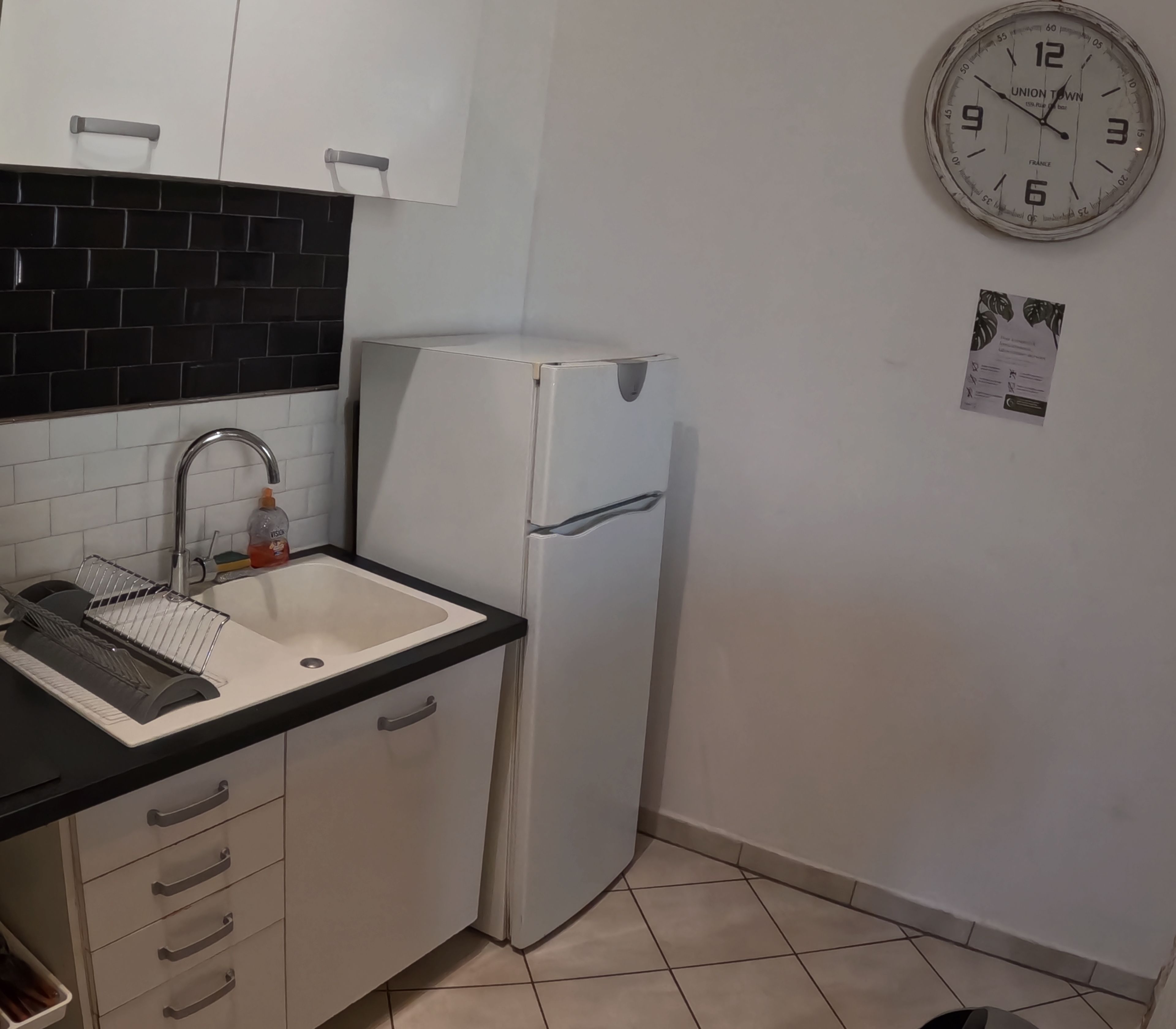 Une cuisine avec un réfrigérateur blanc, un évier avec un égouttoir et une horloge murale.
