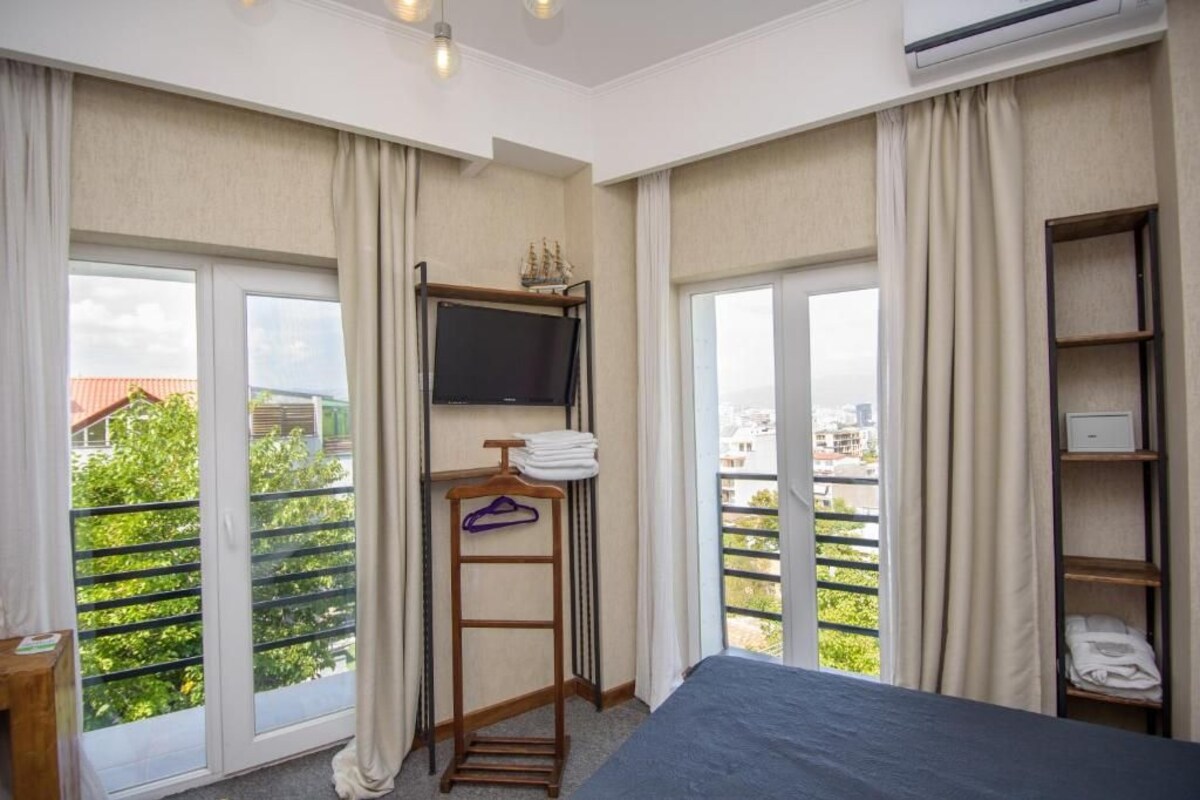 Een hotelkamer met een bed, een aan de muur bevestigde televisie, een balkon met een hekwerk en een raam met gordijnen.