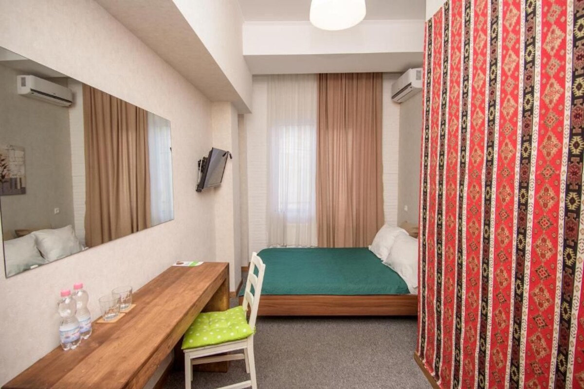 Een hotelkamer met een bed, een bureau, een stoel, een spiegel en een raam met gordijnen.