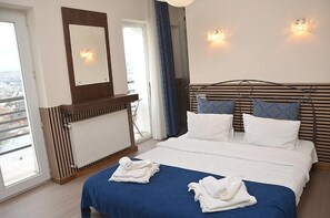 Een hotelkamer met een bed, een raam met uitzicht, een radiator en een spiegel aan de muur.