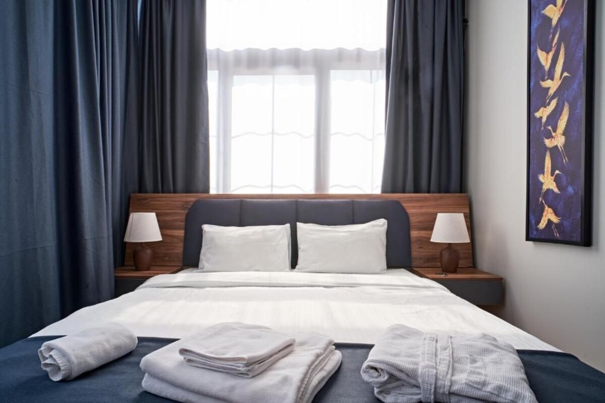 Een hotelkamer met een bed, twee bedlampen, een raam met gordijnen en een kunstwerk aan de muur.