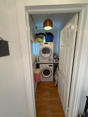 A laundry room with two stacked washing machines, a drying rack, and a hanging light fixture. - Aldwick Avenue, Bognor (West Sussex)
