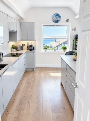 A modern kitchen with white cabinetry, a built-in oven, and a window overlooking a deck. - Aldwick Avenue, Bognor (West Sussex)