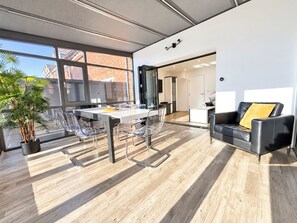 Un salon moderne avec un coin repas, de grandes fenêtres et une vue sur l’extérieur.