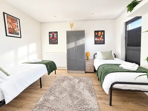 Une chambre avec deux lits, une armoire, un radiateur et des affiches accrochées au mur.