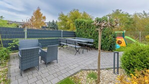 Un patio al aire libre con una mesa y sillas para comer, rodeado por un bajo muro de ladrillo y follaje.