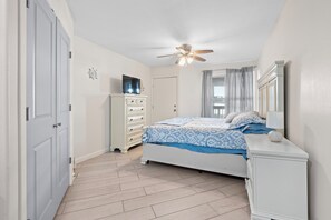 Une chambre à coucher avec un lit, une commode, un téléviseur posé sur un meuble et un ventilateur de plafond.